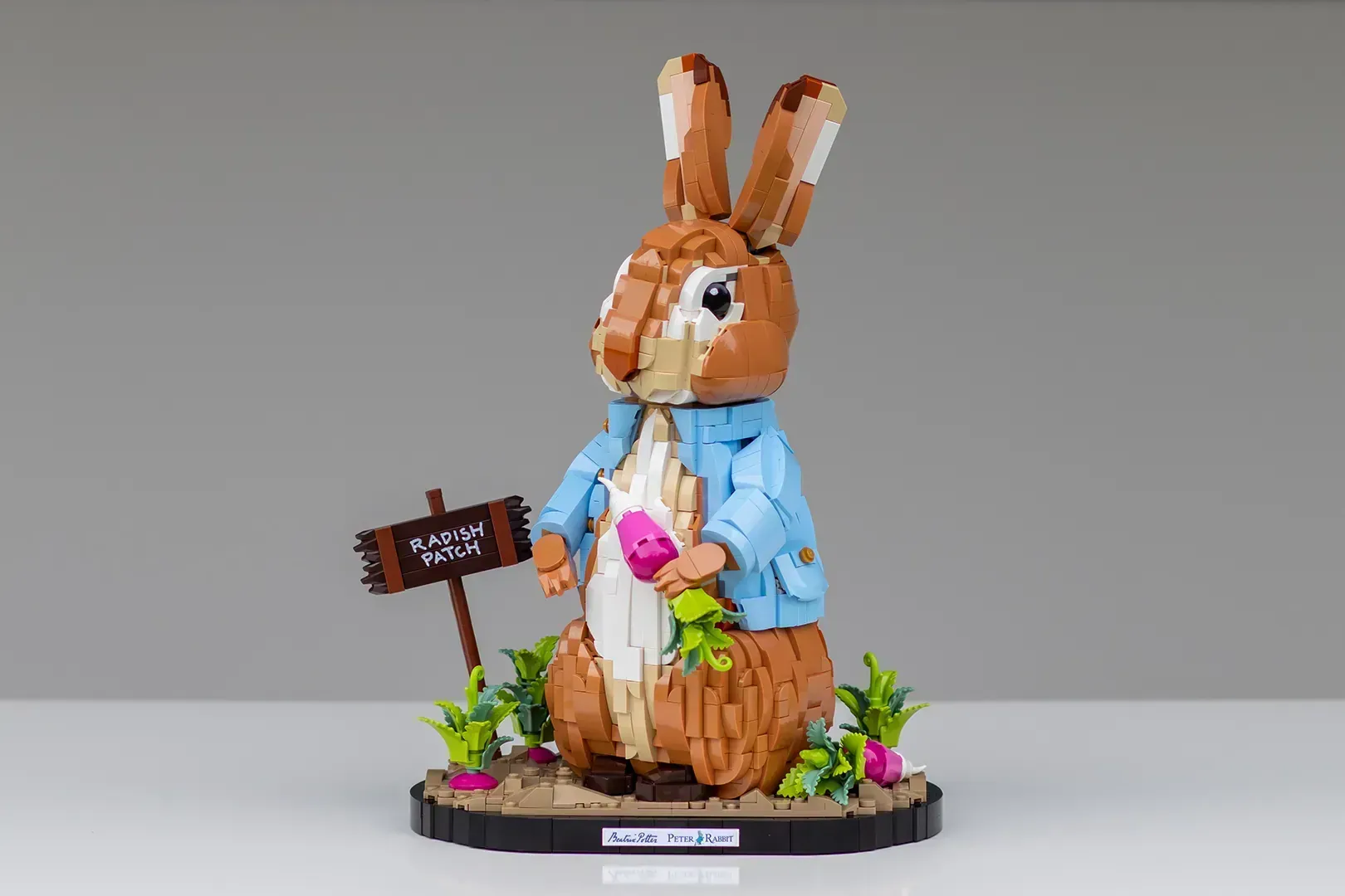 LEGO Ideas Peter Rabbit set with brown rabbit minifigure in blue jacket holding vegetables, standing in garden setting.
