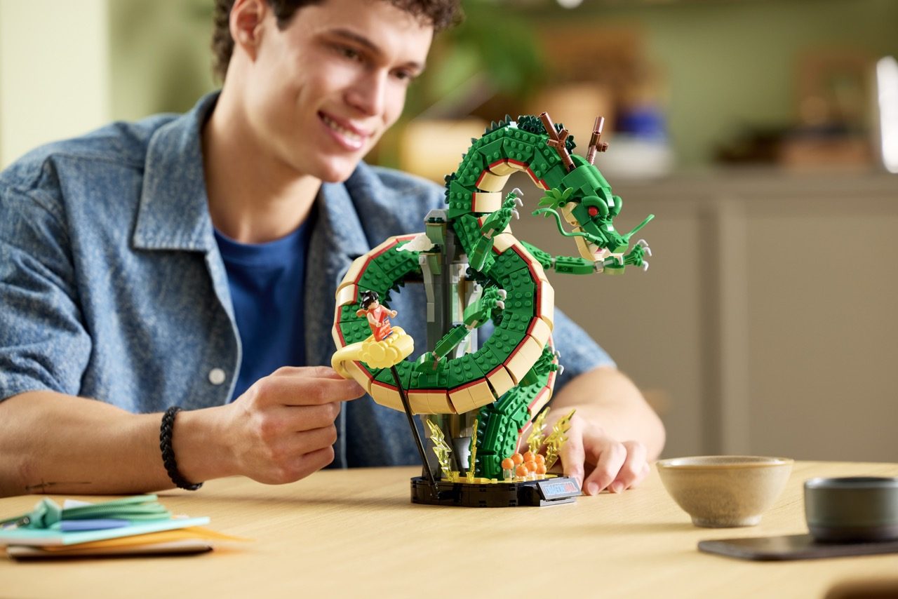 Young boy displaying LEGO Dragon Ball Shenron set with green dragon figure and gold accents on wooden table.
