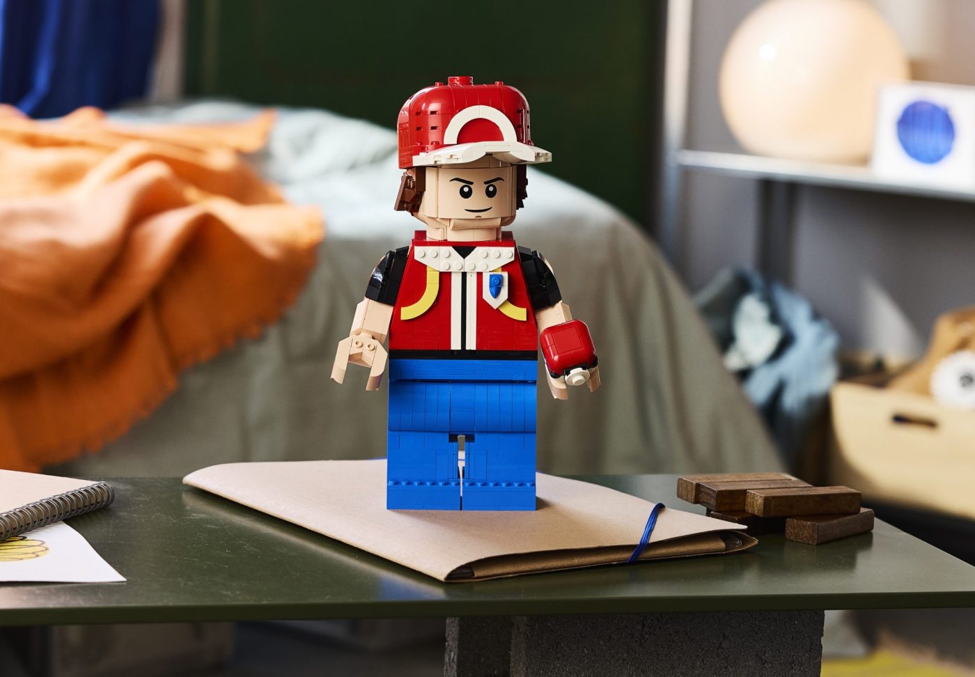 LEGO Pokémon minifigure in red cap and jacket displayed on notebook at desk.
