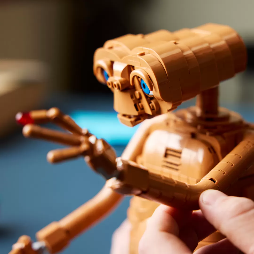 LEGO E.T. figure with glowing blue heart, tan brick construction, articulated arms and fingers, held in hand against blue …
