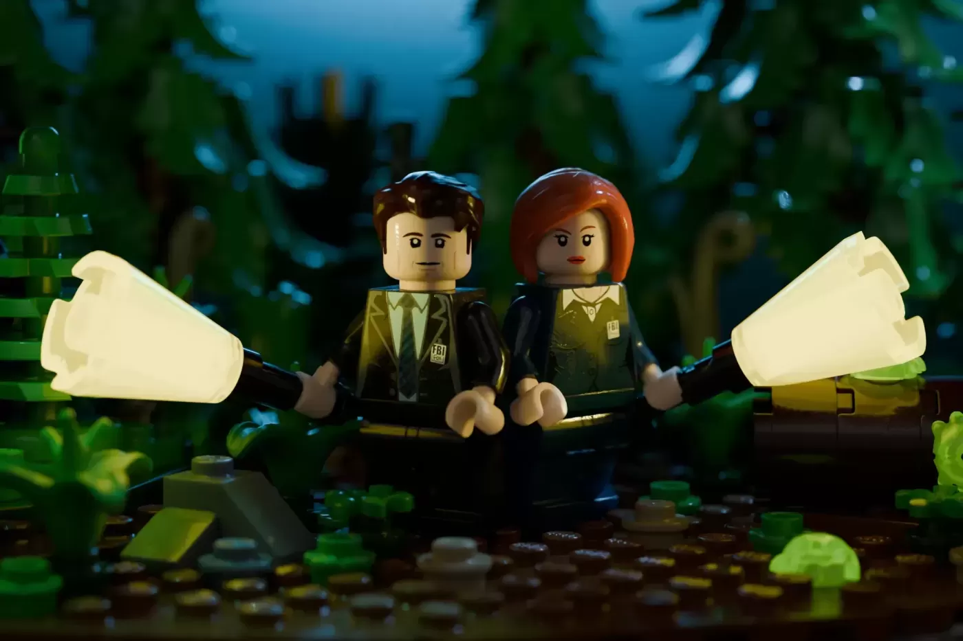 LEGO minifigures of FBI agents with glowing flashlights in a forest setting with alien spacecraft backdrop.