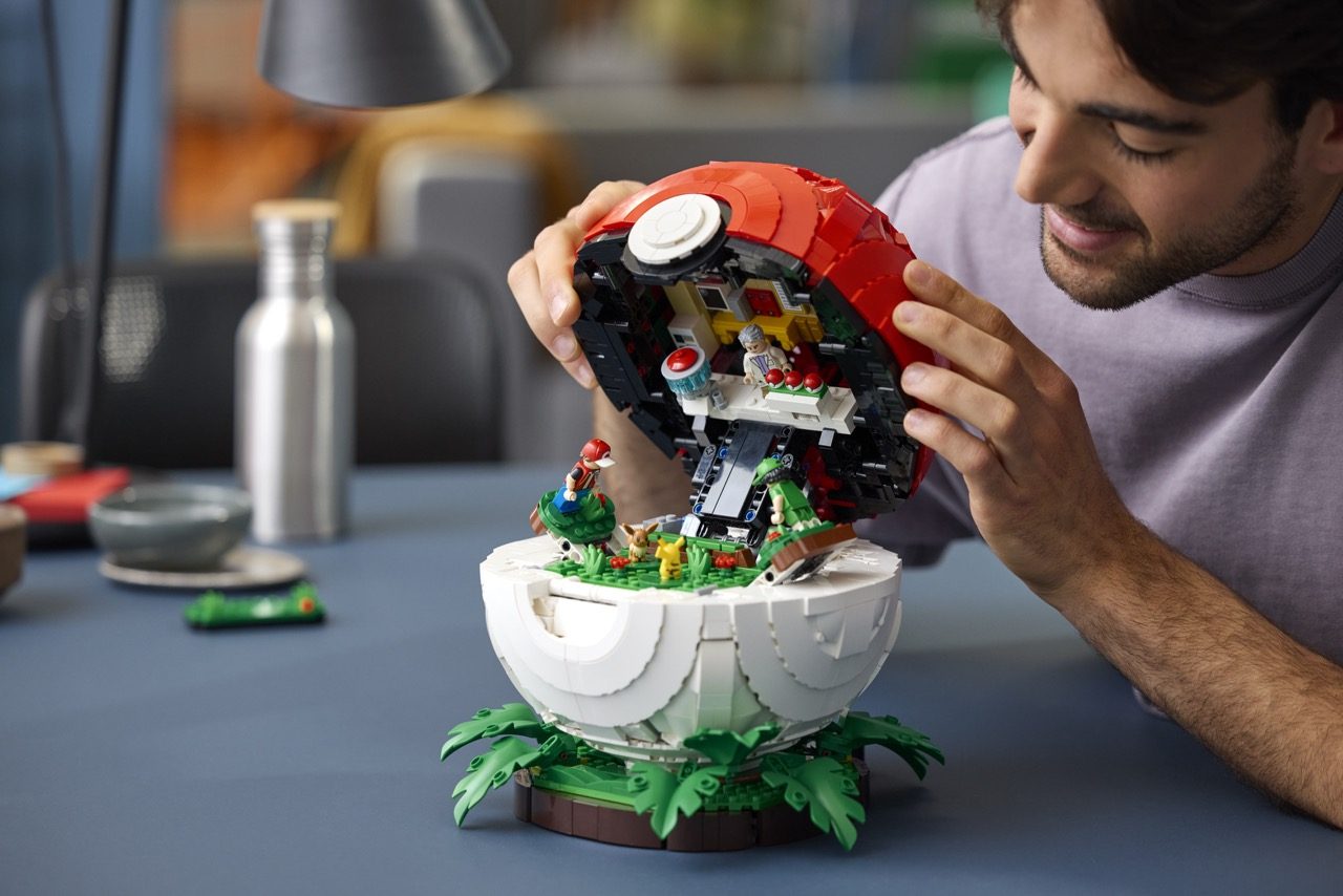 Man assembling red and white LEGO Pokéball set with green plant base and minifigures inside.