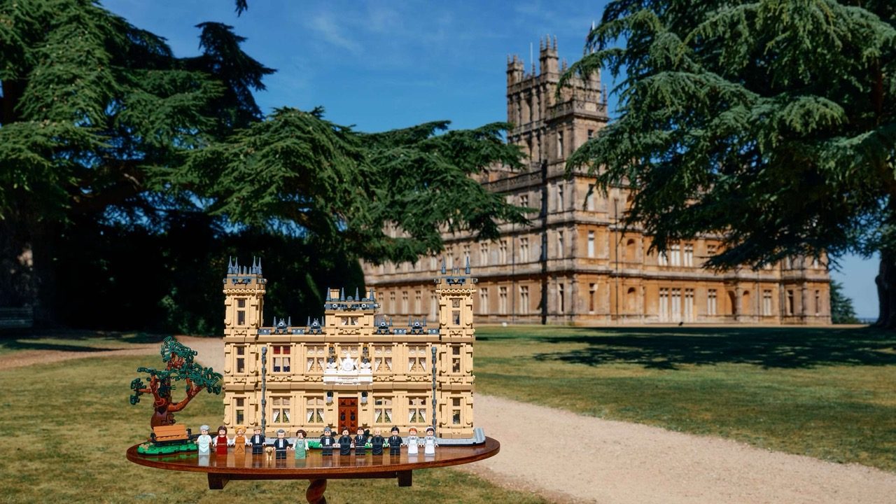 LEGO Downton Abbey set displayed outdoors with Highclere Castle in background and minifigures arranged around base.