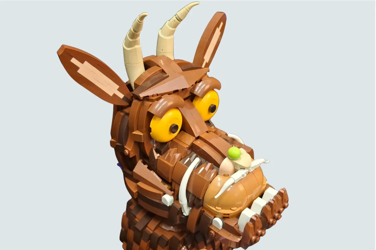 LEGO Gruffalo figure with yellow eyes, horns, and brown body holding a green apple, displayed against white background.