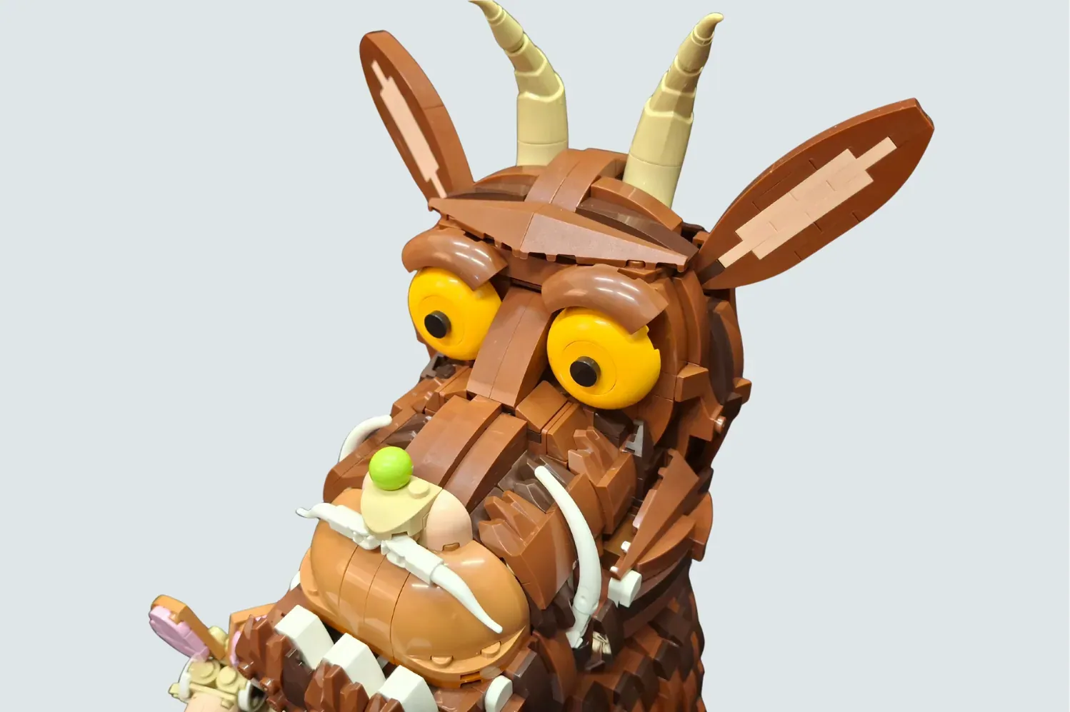 LEGO Gruffalo figure with yellow eyes, tan horns, brown body, holding a green apple and purple brush piece.