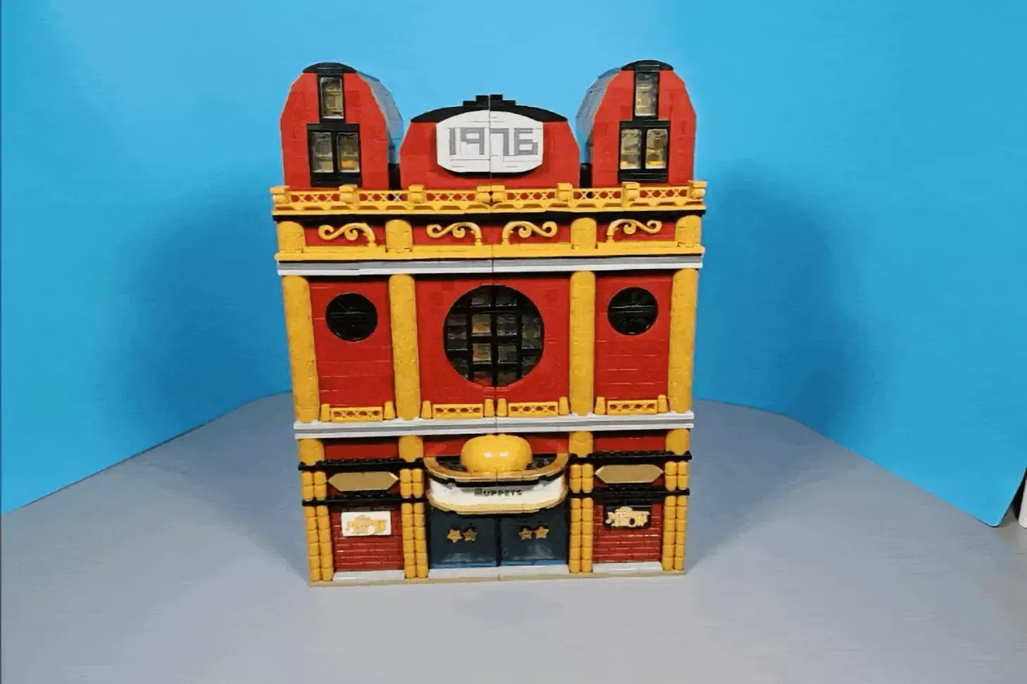 LEGO Muppet Theatre building with red and yellow facade, arched roof, and "1976" marking on blue background.