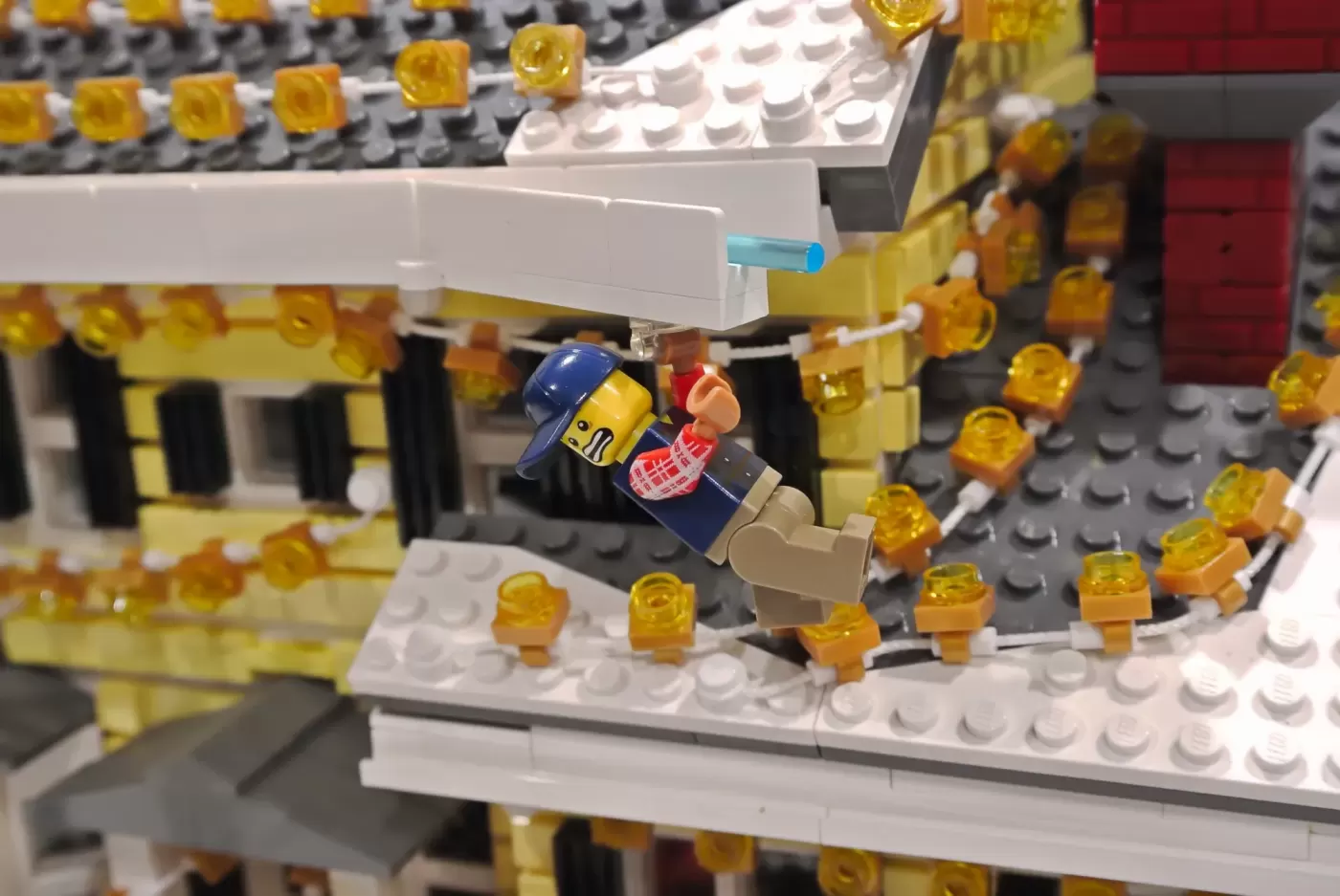LEGO minifigure slipping on icy roof covered in golden lights during Christmas Vacation house display.