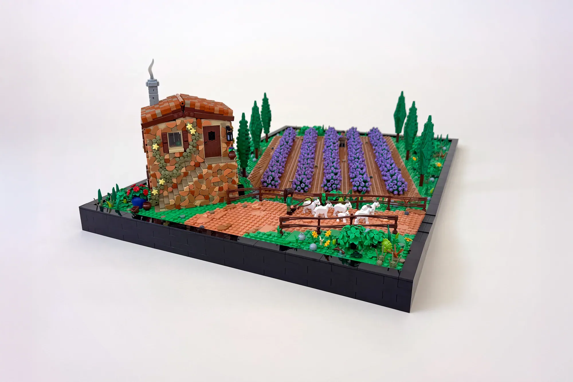 LEGO lavender field scene with brick cottage, purple flower rows, cypress trees, and benches on display base.