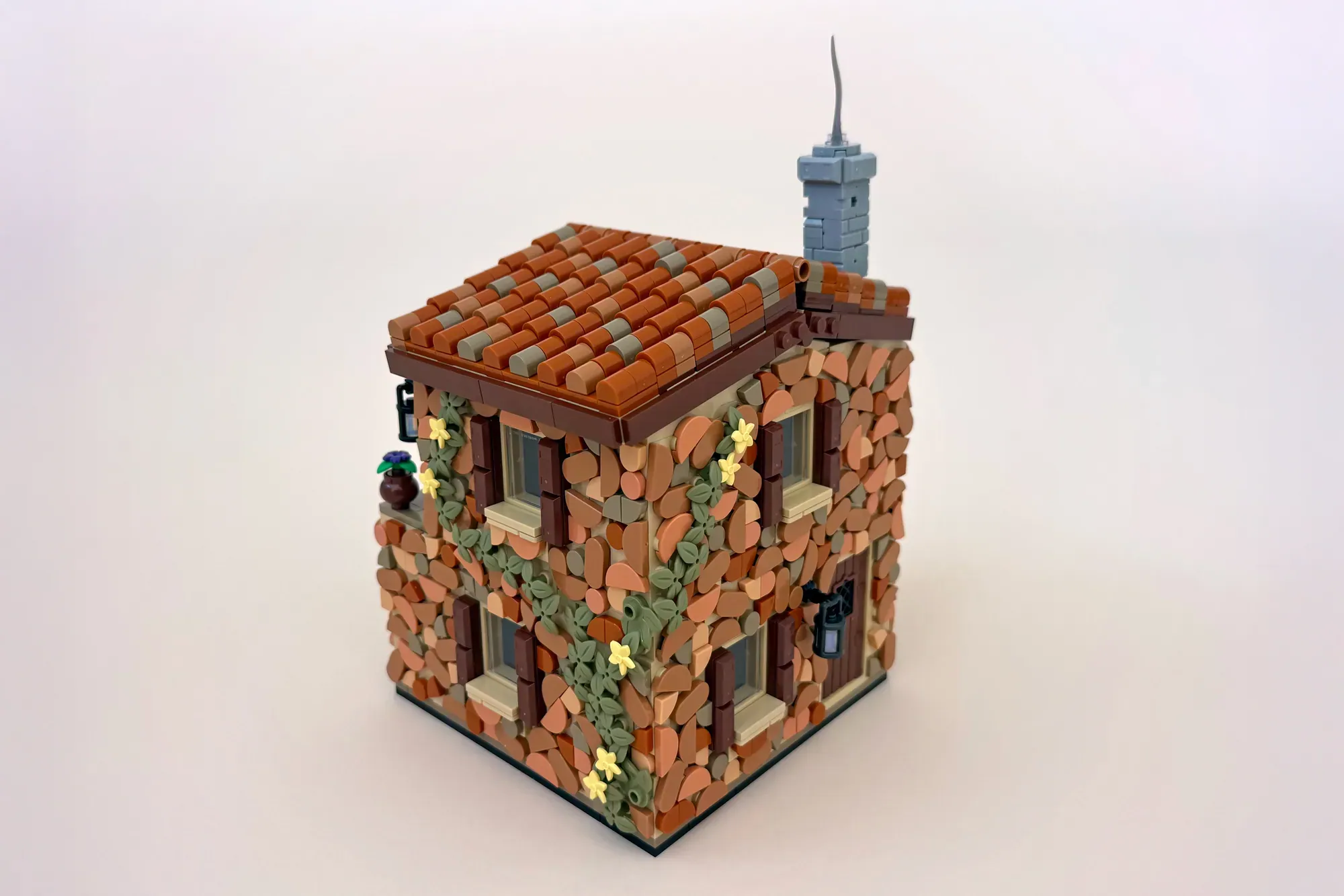 LEGO brick cottage with ivy-covered walls, terracotta roof tiles, and a blue stone chimney.