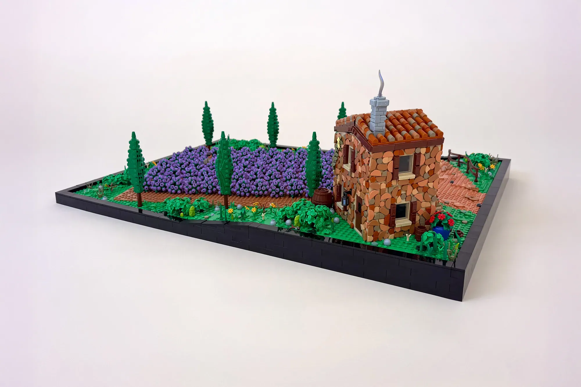 LEGO lavender field diorama with stone cottage, purple flower wall technique, cypress trees, and black base platform.