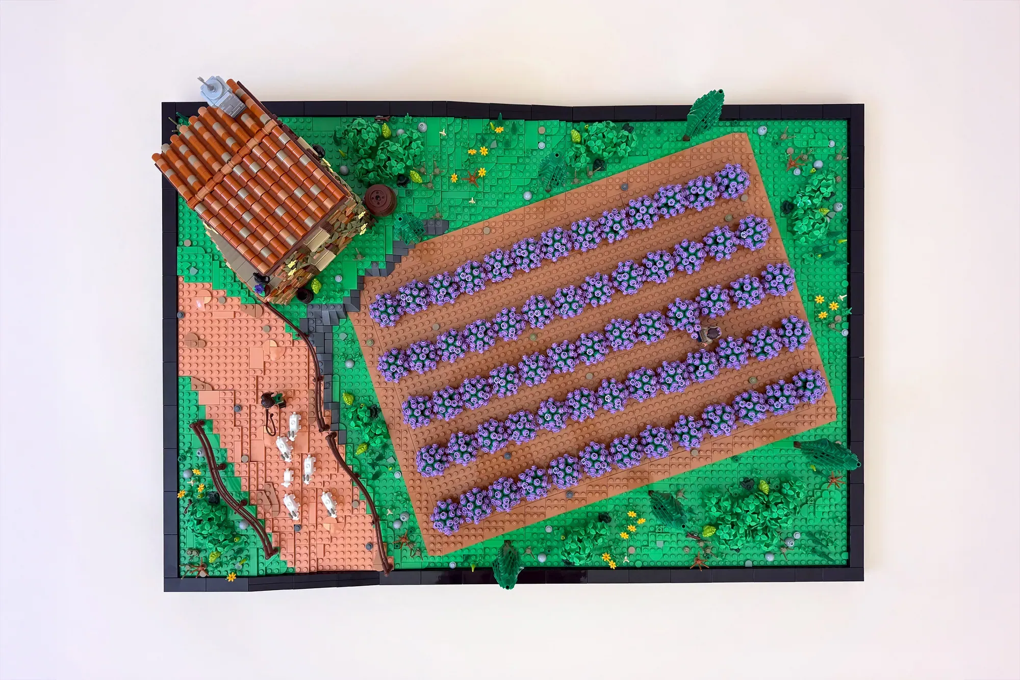 LEGO lavender field display with purple flowers in rows, brown barn, green landscape, and trees on black base board.