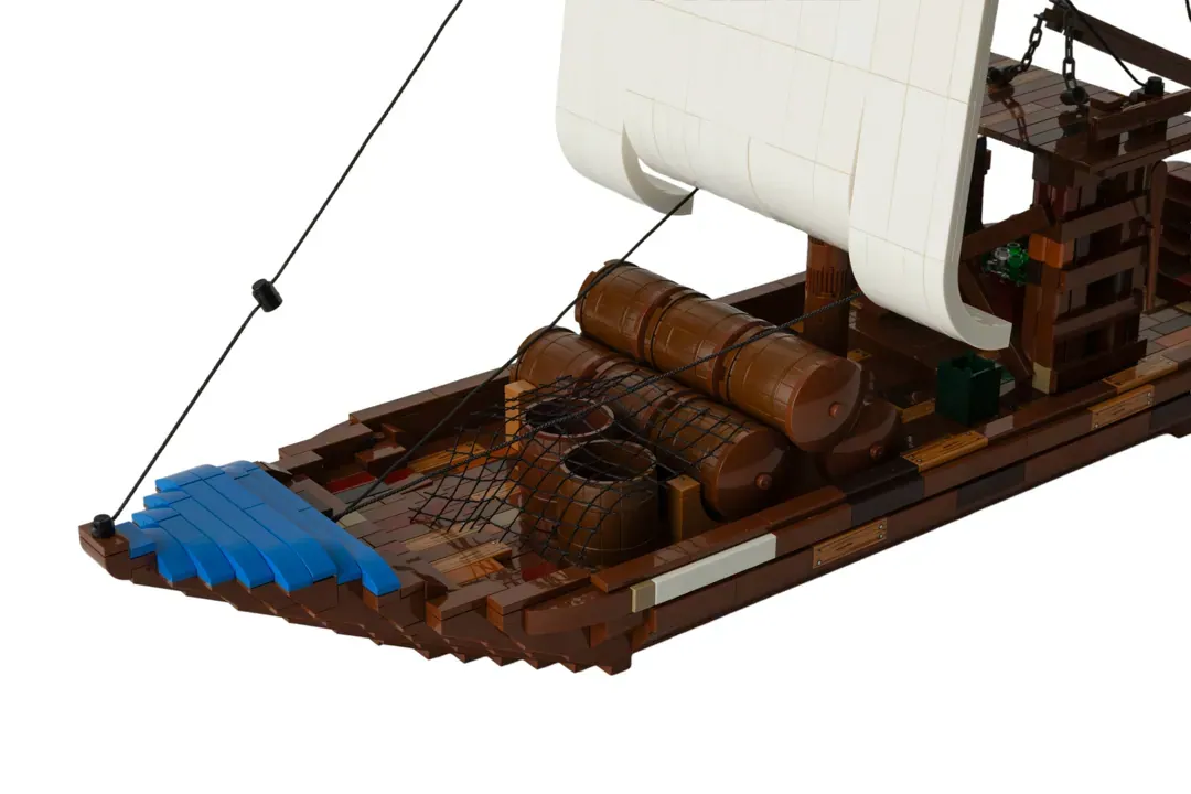 LEGO Barco Rabelo model with white sail, wooden hull, blue cargo, and brown barrels on display.