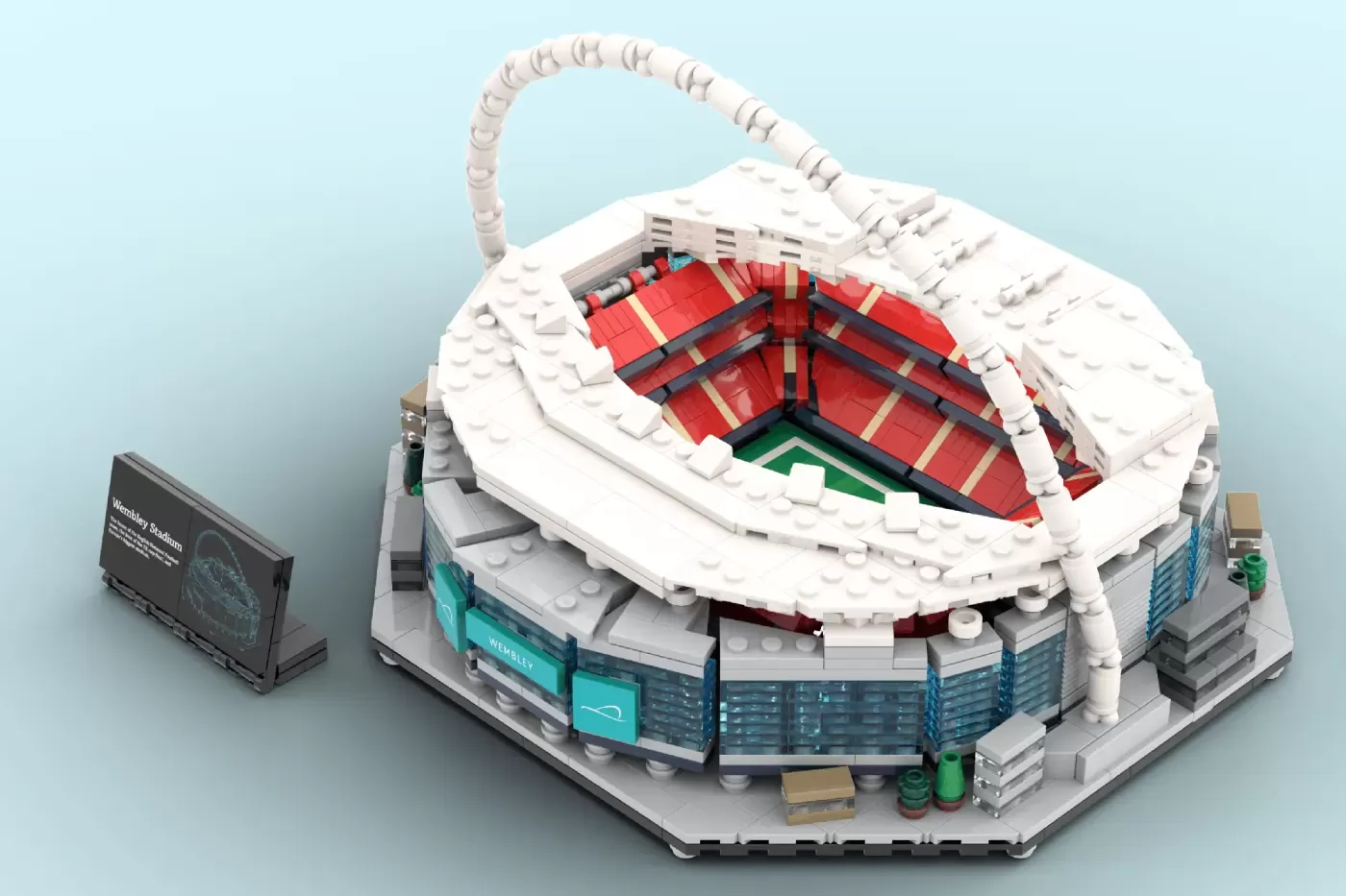 LEGO Wembley Stadium model featuring iconic white arch, red seating, green pitch, and turquoise base with informational pl…