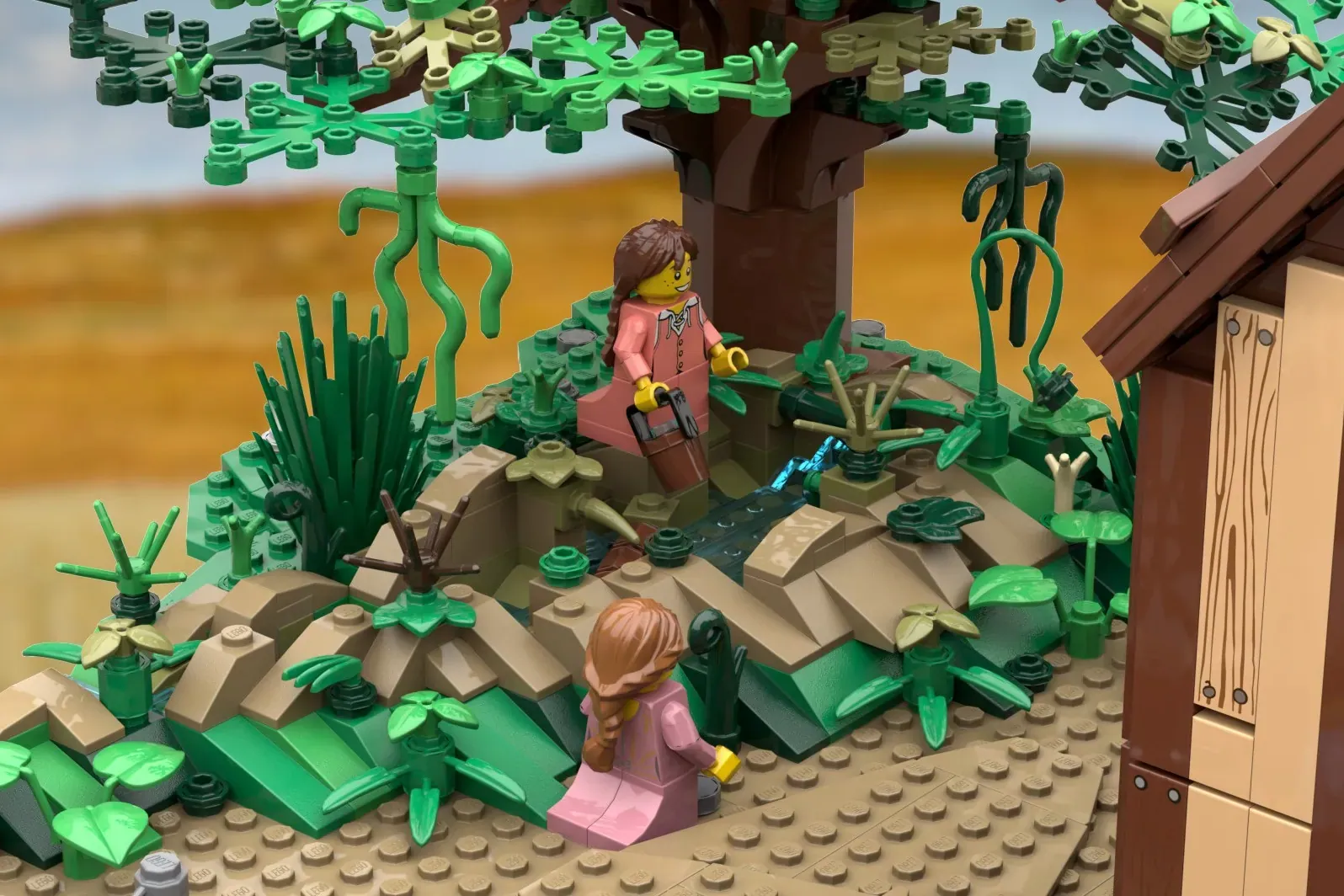 LEGO prairie scene with two minifigures in pink dresses among green plants and wooden structures under a large tree.