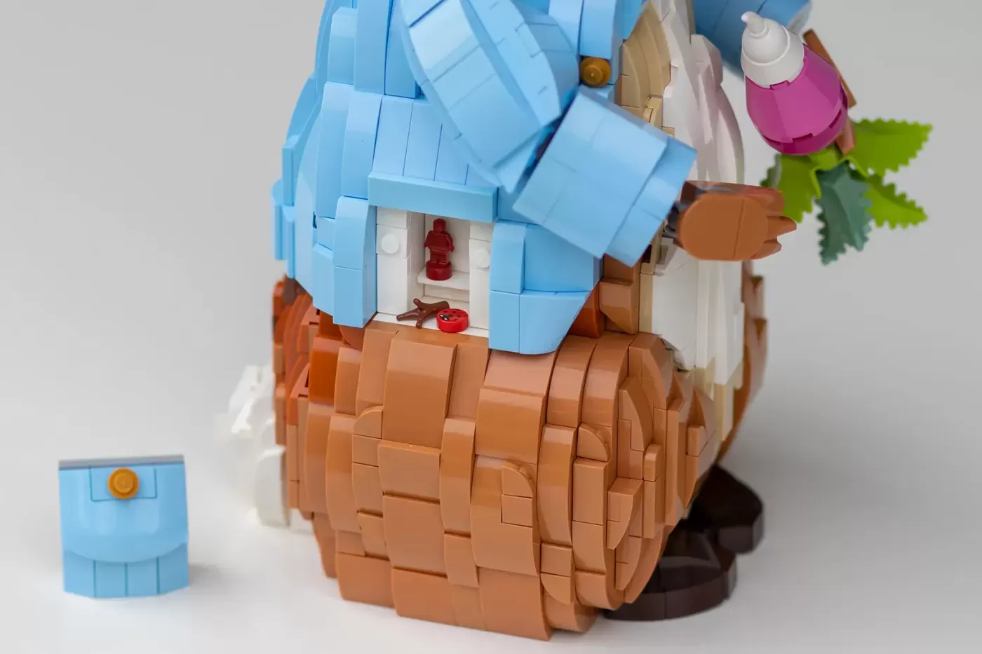 LEGO build of a mushroom house with blue roof, brown trunk base, and green foliage, featuring a red minifigure inside.
