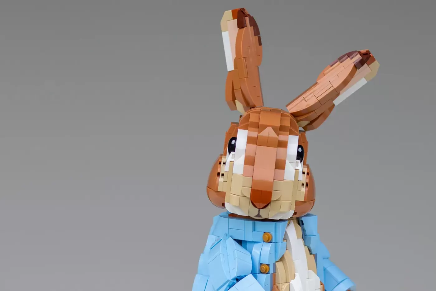 LEGO brick-built Peter Rabbit figure with brown fur, white face, and blue jacket against gray background.