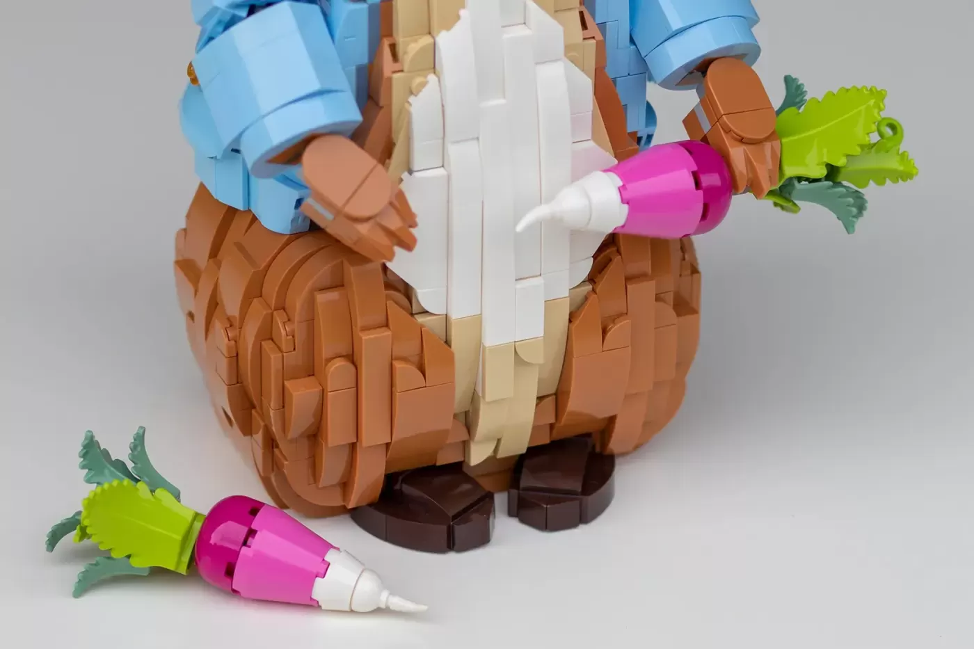 LEGO brick-built Peter Rabbit figure holding a carrot, wearing blue jacket, with additional carrots nearby.