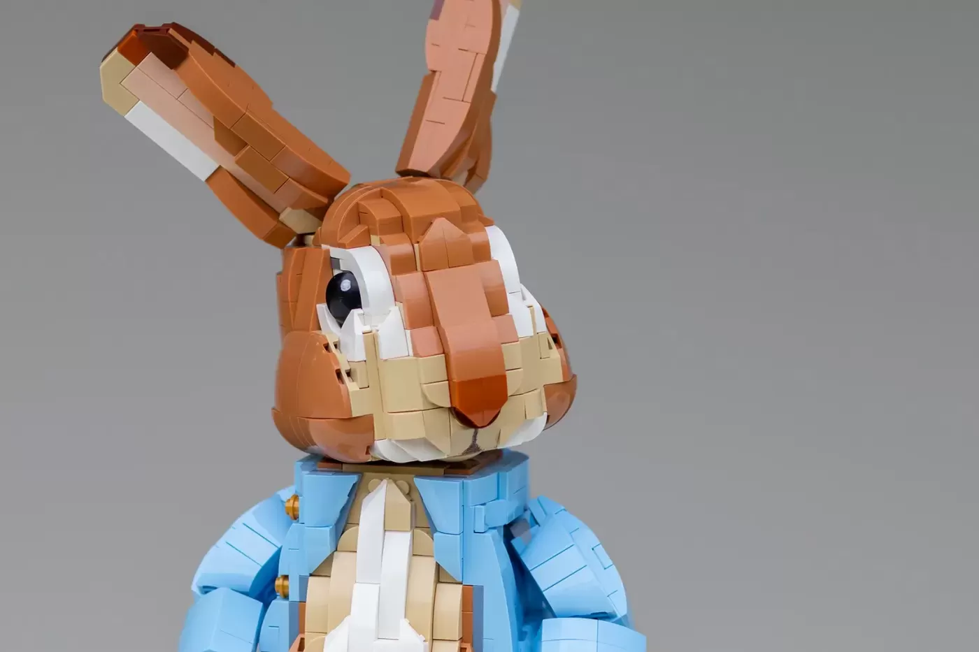 LEGO brick model of Peter Rabbit in blue jacket with brown ears and white chest detail against gray background.