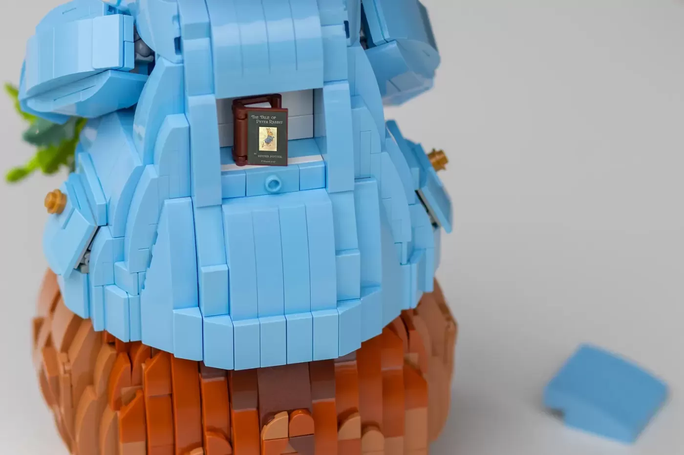 LEGO brick model of a blue cottage with brown base, featuring "The Tale of Peter Rabbit" book inside.