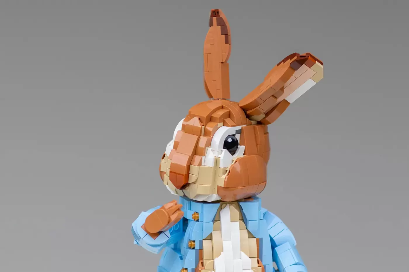 LEGO brick-built Peter Rabbit figure with brown fur, blue jacket, and articulated limbs against gray background.