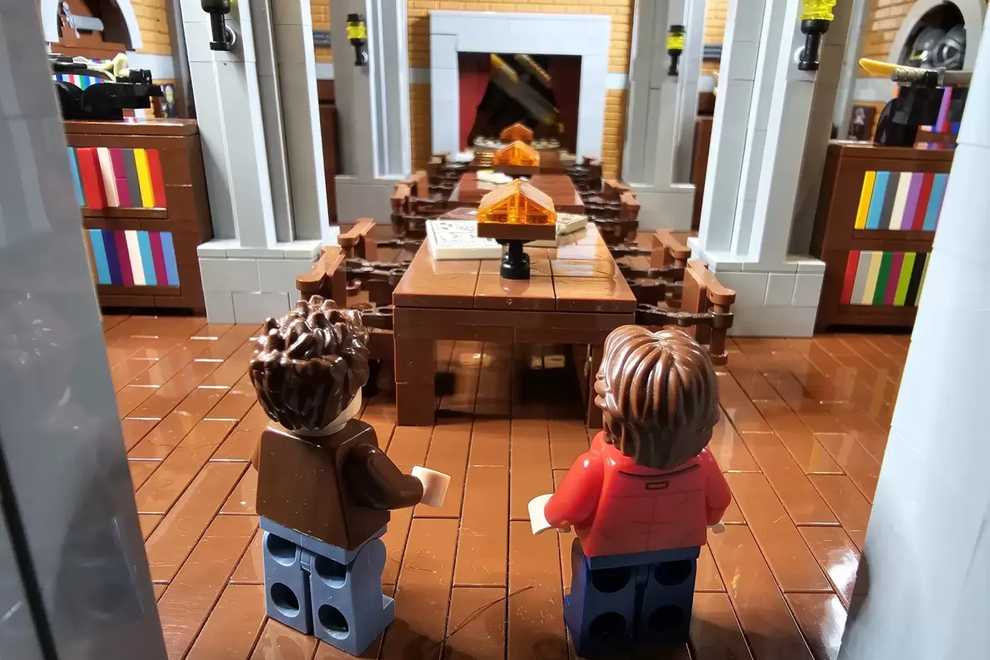 LEGO bunker interior with two minifigures facing desks, fireplace, and colorful bookshelves in perspective view.