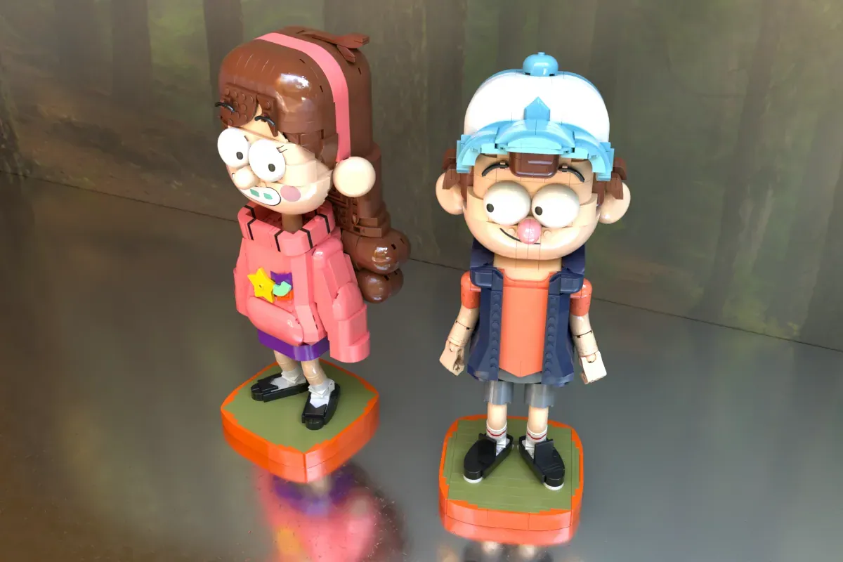 Two LEGO figures of Mabel and Dipper from Gravity Falls standing on green and orange bases against a gray backdrop.