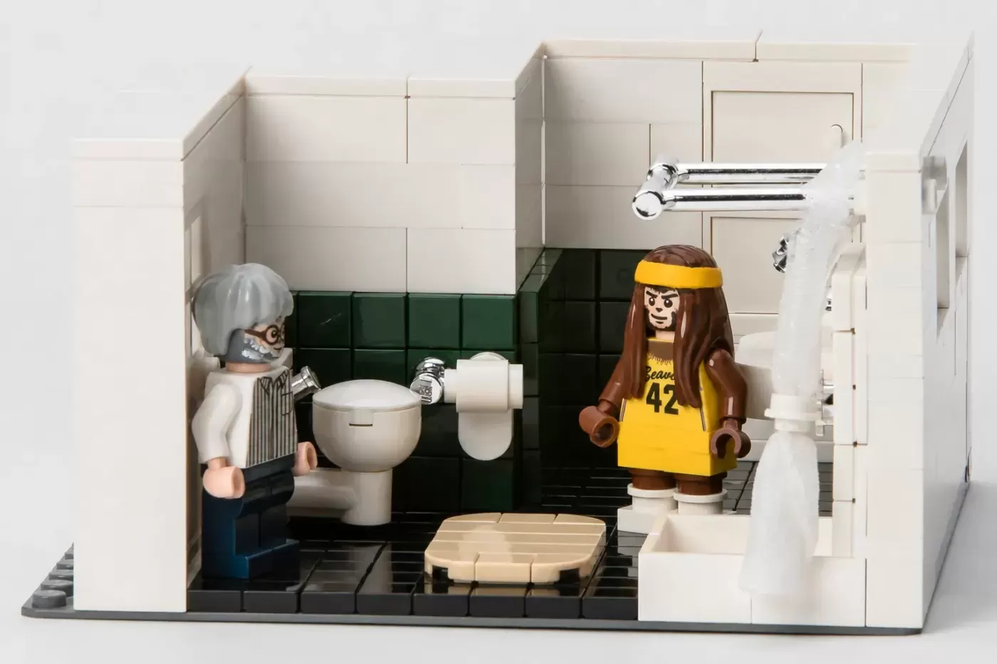 LEGO bathroom set with elderly woman and teen in yellow jersey, featuring toilet, sink, and black tile flooring.