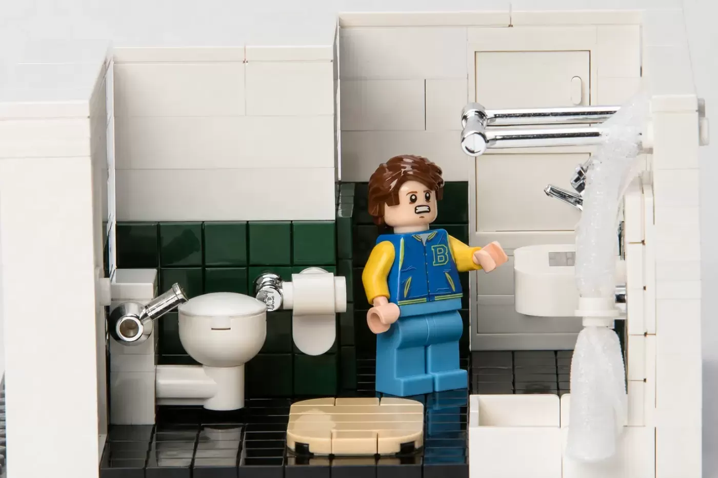 LEGO minifigure in blue and yellow jacket stands in detailed bathroom set with toilet, sink, and shower fixtures.